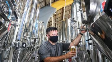 homem tira cerveja de equipamento na fábrica #paratodosverem