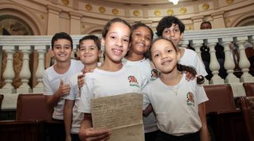 crianças com uniforme do município posam para foto sorrindo na sala princesa isabel. #paratodosverem