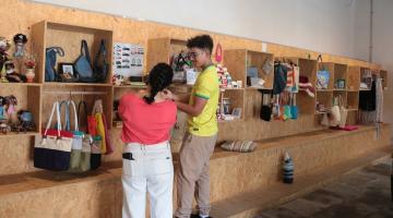 homem e mulher estão de costas para a foto e de frente para prateleira onde estão expostos produtos artesanais. #paratodosverem 