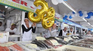 funcionárias seguram balões formando número 38 ao lado de peixes à venda #pracegover 