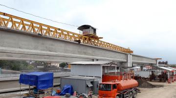 Vista geral da ponte já com algumas vigas. Homens estão trabalhando na área entorno. #Pracegover