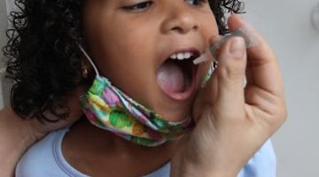 mão está pingando gota da vacina sabin na boca de uma menina. #paratodosverem