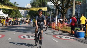 ciclista está pedalando em avenida da orla. Ao fundo há várias pessoas. #paratodosverem