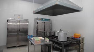 cozinha com fogão industrial, coifa, mesa e geladeiras. #paratodosverem