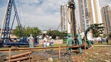 homens estão trabalhando em canteiro de obras em meio a máquinas de fundação. #paratodosverem