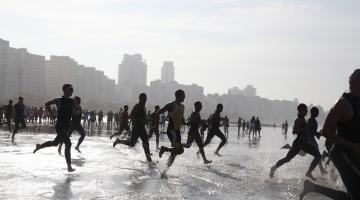 Pessoas correndo na direção do mar em competição #paratodosverem