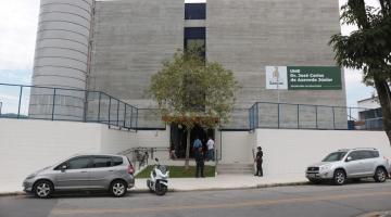 fachada da escola com árvore na entrada. há dois carros e uma mota estacionados na frente. A escola tem um placa de identificação. #paratodosverem 