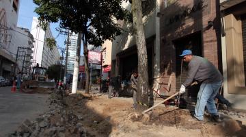 Homem trabalha na reforma de calçada de rua. Há pedras soltas e terra aparente. #Pracegover