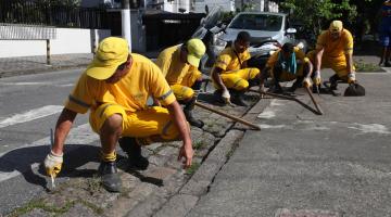 grupo de operários está ajoelhado capinando #pracegover 