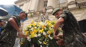 Imagem da Padroeira é carregada por dois soldados em frente à Prefeitura. A imagem está cercada de flores. #Pracegover