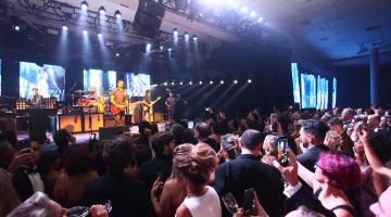 Baile com pessoas dançando em pista. À frente tem um palco com um cantor. #Pracegover