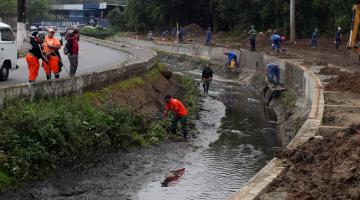 Canal de avenida com talude em manutenção e desassoreamento. # Pracegover