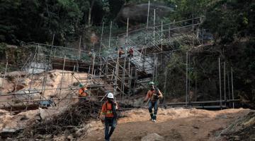 homens estão trabalhando em encosta onde foram instalados andaimes. #paratodosverem