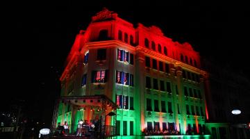 Fachada de hotel iluminada em vermelho e verde, cores típicas do Natal, para show musical. #Pracegover
