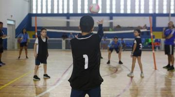 menino de costas para a foto está no início da quadra lançando a bola para o outro lado da rede. #paratodosverem 