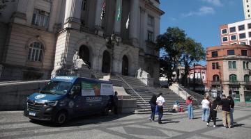 van da guarda municipal está parada na praça mauá em frente ao Paço. Ao lado, vários pacotes de roupas e pessoas circulando. #paratodosverem