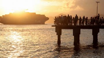 pessoas estão no deck do pescador vendo saída de navios. #paratodosverem 