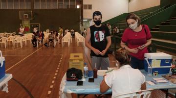 jovem e mulher são atendidos em ginásio para vacinação #paratodosverem