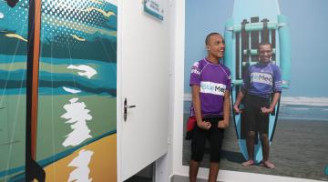 Rapaz com deficiência posa ao lado de sua foto impressa na parede da escola #pracegover 