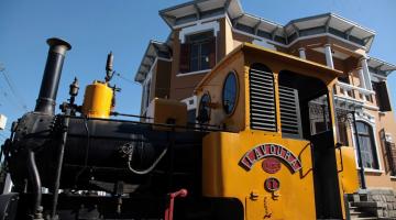 antiga locomotiva parada na frente de prédio. #paratodosverem 