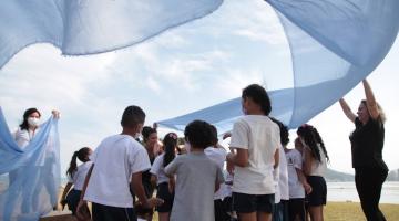 crianças brincam em jardim envoltas de pano azul #paratodosverem