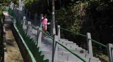 mulher está descendo escadaria no morro. Há vegetação do lado direito da foto. #paratodosverem 