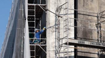 homem está em andaime reparando fachada de prédio. #paratodosverem 