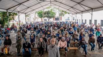 Homem na frente  conversa com muitas pessoas em um galpão #paratodosverem