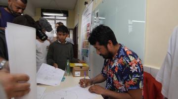 Artista peruano faz desenho observado por estudantes. #paratodosverem