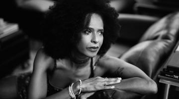 a cantora Izzy Gordon sentada numa poltrona olhando para trás e com os braços no encosto. #paratodosverem