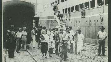 Imagem antiga. Japoneses desembarcam em Santos. Navio está encostado no cais. #Pracegover