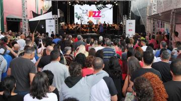 grande público assiste apresentação musical no palco ao fundo. #paratodosverem