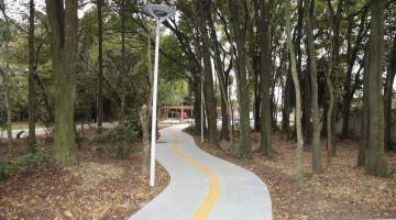 área de caminhada no parque em meio a vegetação, com várias árvores e poste de iluminação 