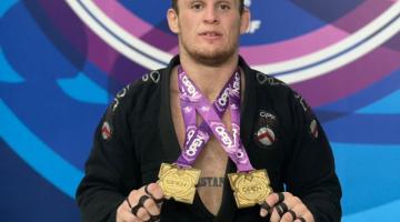 Christiano Tayfour Troisi segura com as mãos as medalhas penduradas no peito. #paratodosverem