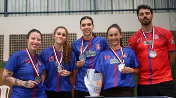 quatro atletas do tênis de mesa feminino seguram suas medalhas e posam atrás do troféu da Cidade. #paratodosverem