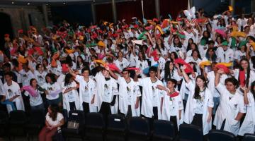 alunos formados de jaleco balançam lenços ao alto #paratodosverem