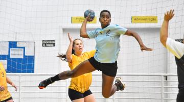 jogadora de handebol pula com a bola para fazer arremesso #paratodosverem