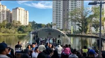 público em primeiro plano, de costas, assistindo apresentação em palco flutuante. #paratodosverem