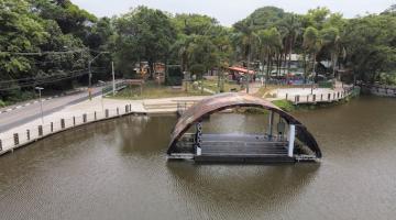 vista aérea da lagoa da saudade, com palco flutuante na água, vegetação e área de lazer ao fundo. #paratodosverem