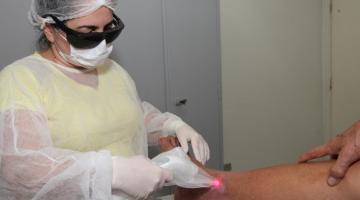 Enfermeira realiza aplicação de laser em pé de paciente. #paratodosverem 