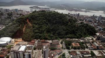 morro ao fundo com marca de escorregamento de encosta. prédios em primeiro plano e o mar ao fundo. #paratodosverem