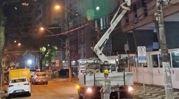 caminhão com braço basculante e um cesto no alto carrega homem que faz troca de luminária no poste. #paratodosverem
