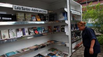 livros dispostos em biblioteca móvel. Uma mulher mexe em uma publicação. #paratodosverem