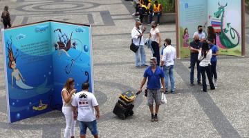 Grandes estruturas em formato de livros montadas na praça. Há pessoas circulando