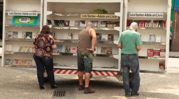 três pessoas estão diante de biblioteca ambulante. Todsos estão de costas para a foto. #paratodosverem