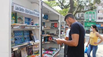 Homem escolhe livro na biblioteca móvel na Praça Mauá. #paratodosverem