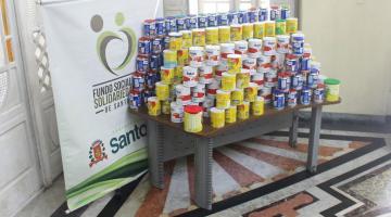 mesa com várias latas de leite em pó empilhadas. ao lado esquerdo, o banner do fundo social de solidariedade