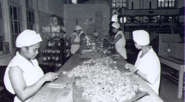 mulheres embrulham balas sobre balcão. Foto antiga em preto e branco. #paratodosverem