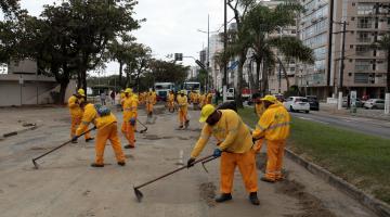 homens uniformizados varrem areia de avenida da orla. #paratodosverem