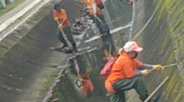 Funcionários da limpeza removem mato de paredes internas do canal. #pracegover